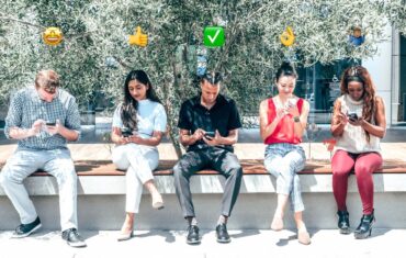 5 osób siedzących i patrzących na telefony, nad każdą z nich widoczne emoji