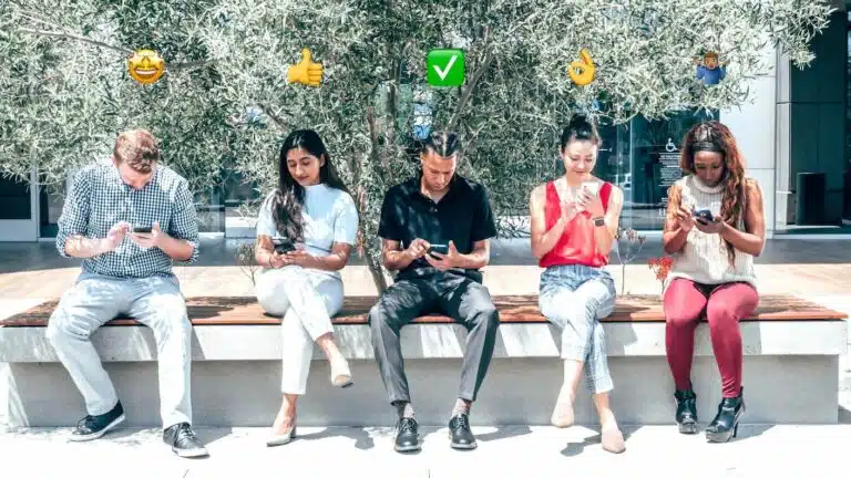 5 osób siedzących i patrzących na telefony, nad każdą z nich widoczne emoji