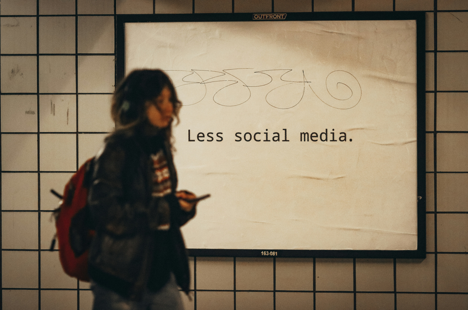 Kobieta przechodzi przed banerem. Na banerze znajduje się napis Less Social Media.