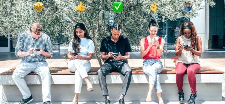 5 osób siedzących i patrzących na telefony, nad każdą z nich widoczne emoji